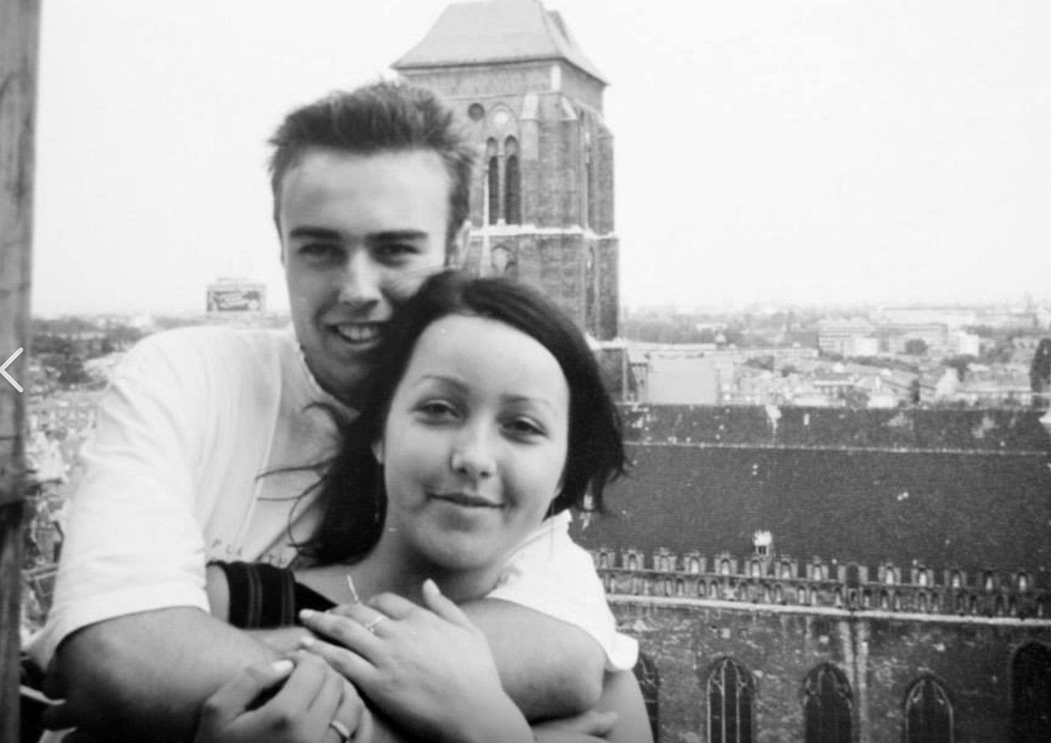 A vintage black and white photograph showing a couple embracing with a city tower in the background.