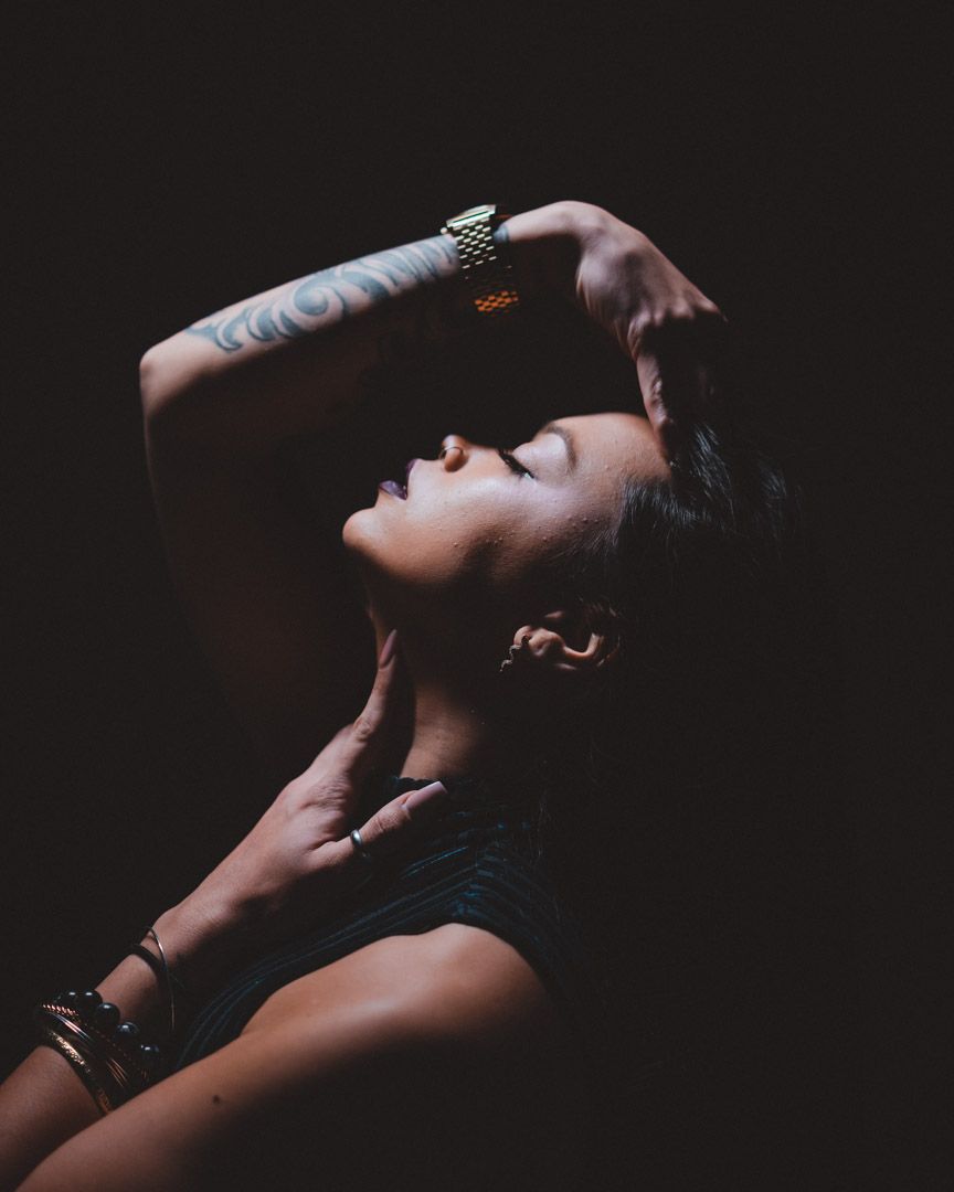 Dramatic low-key portrait with arms raised against dark background.