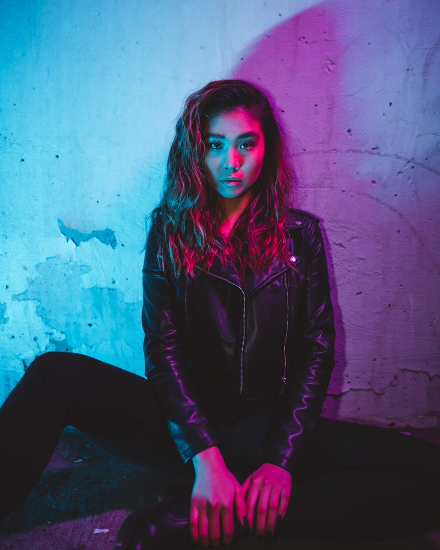 Moody portrait with blue and pink neon lighting against textured wall.