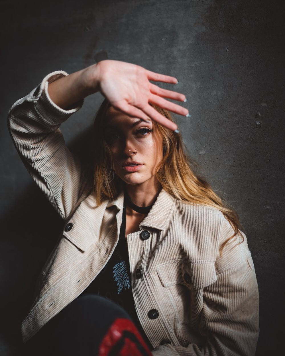 Dramatic portrait with hand gesture against dark wall creating shadow and contrast.