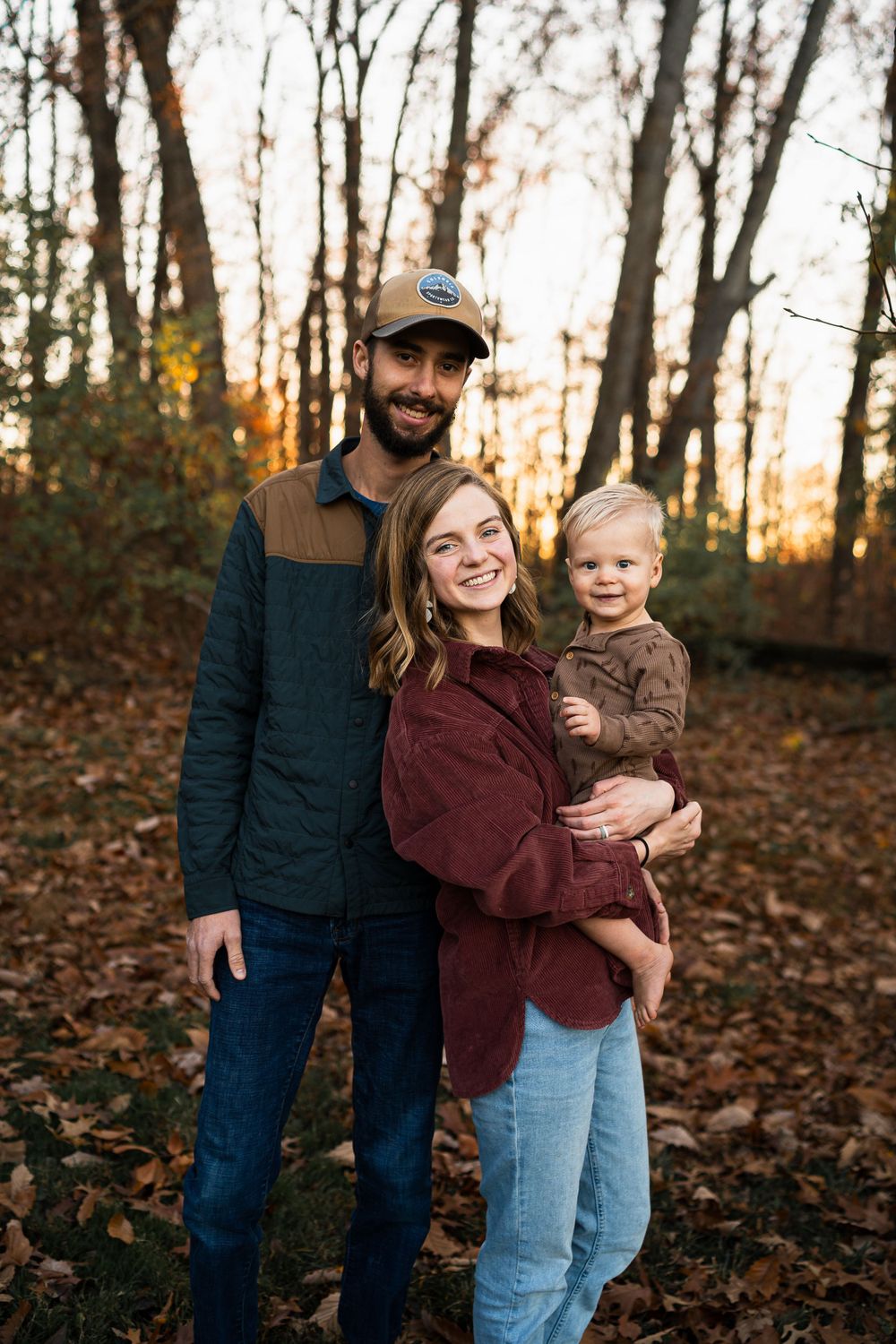 A heartwarming autumn family portrait in the woods with fallen leaves surrounding them.