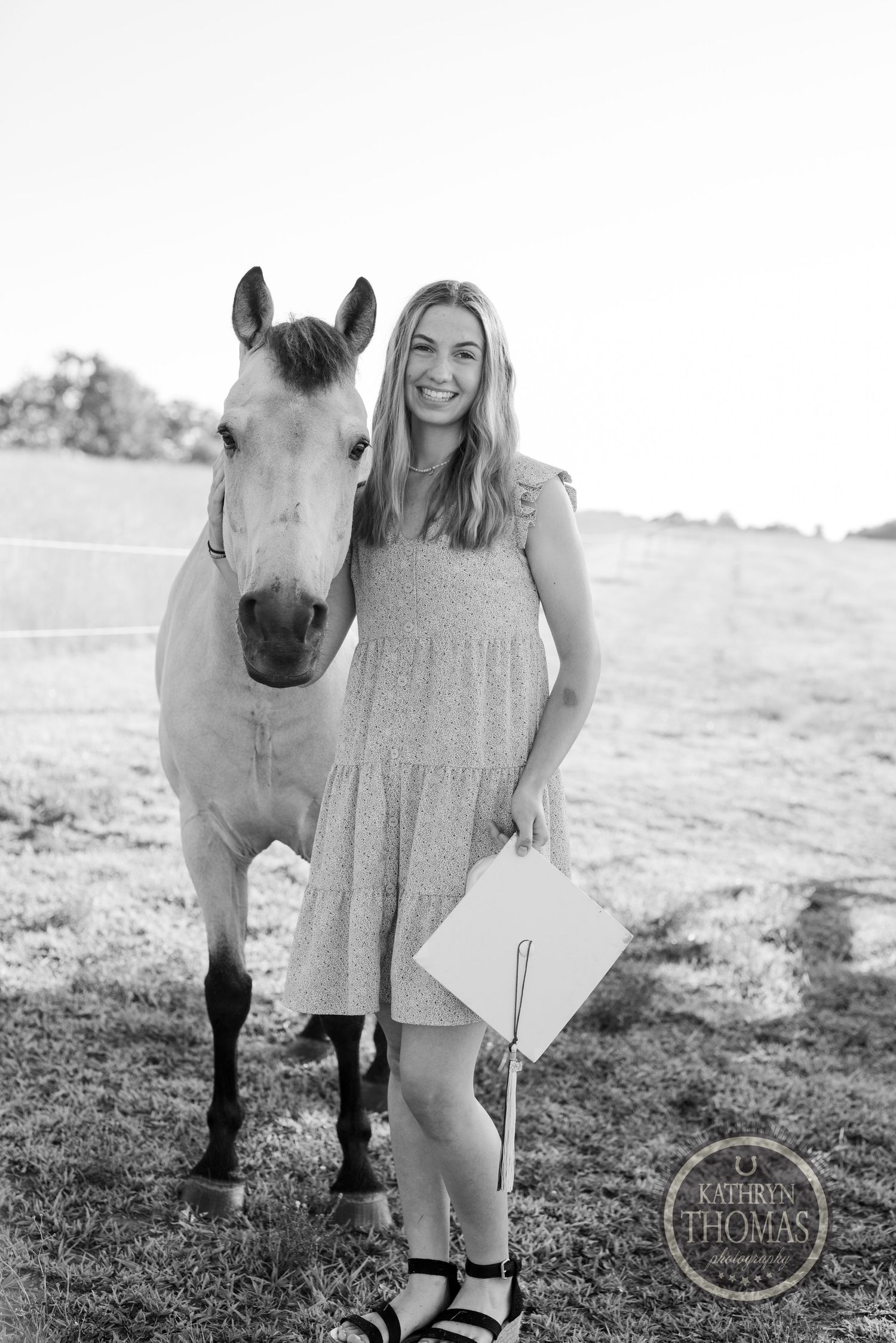 A light-colored horse poses with someone wearing a casual summer dress in a black and white countryside photo.