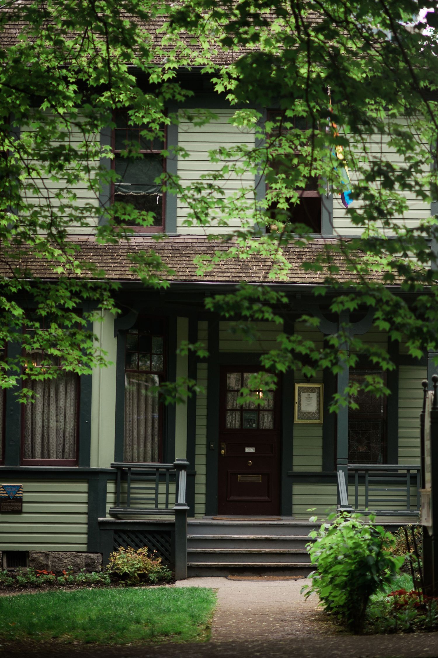 Historic Victorian-style house with green trim and leafy branches framing the front porch entrance.