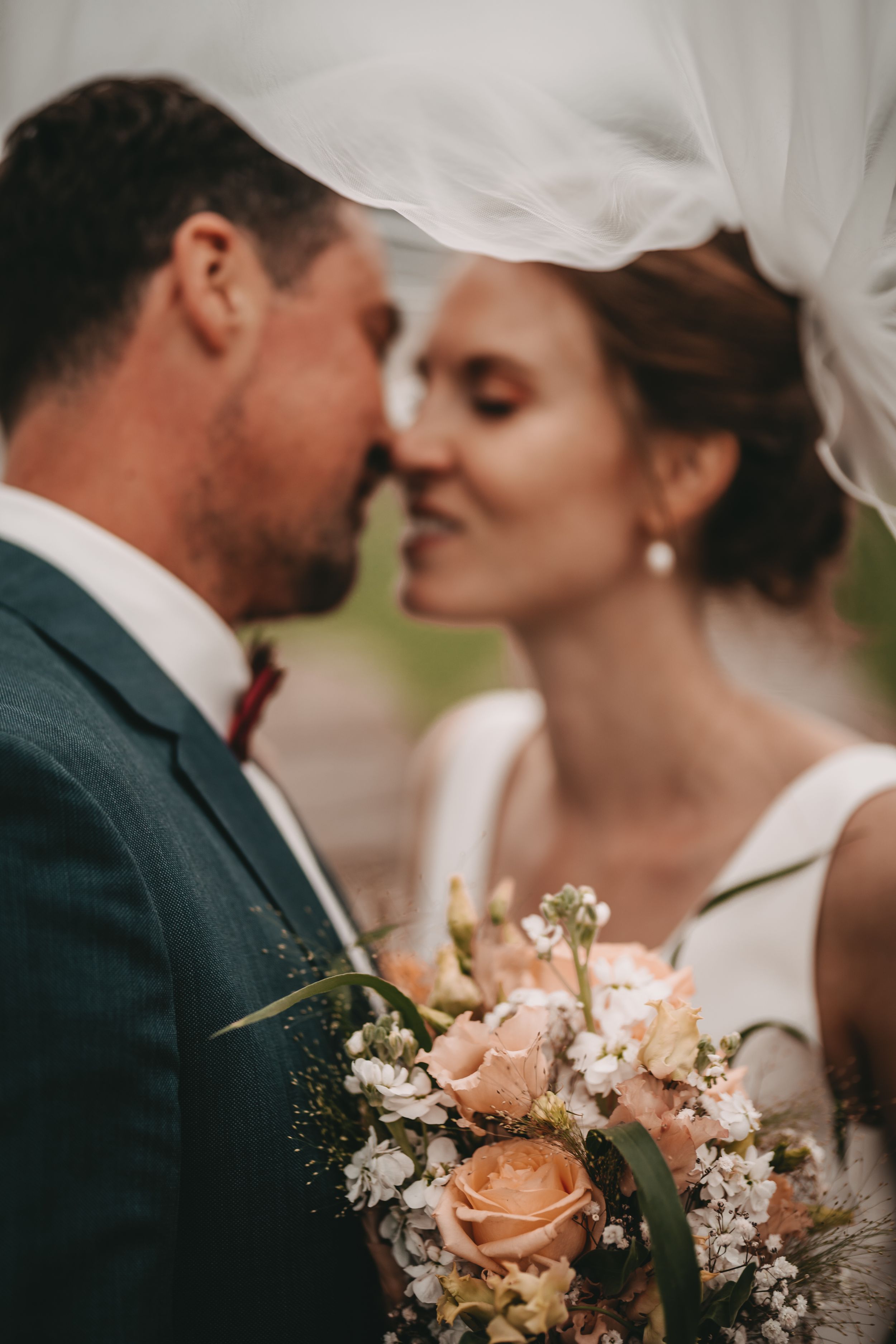 Wedding couple with peach and white floral bouquet in outdoor setting.