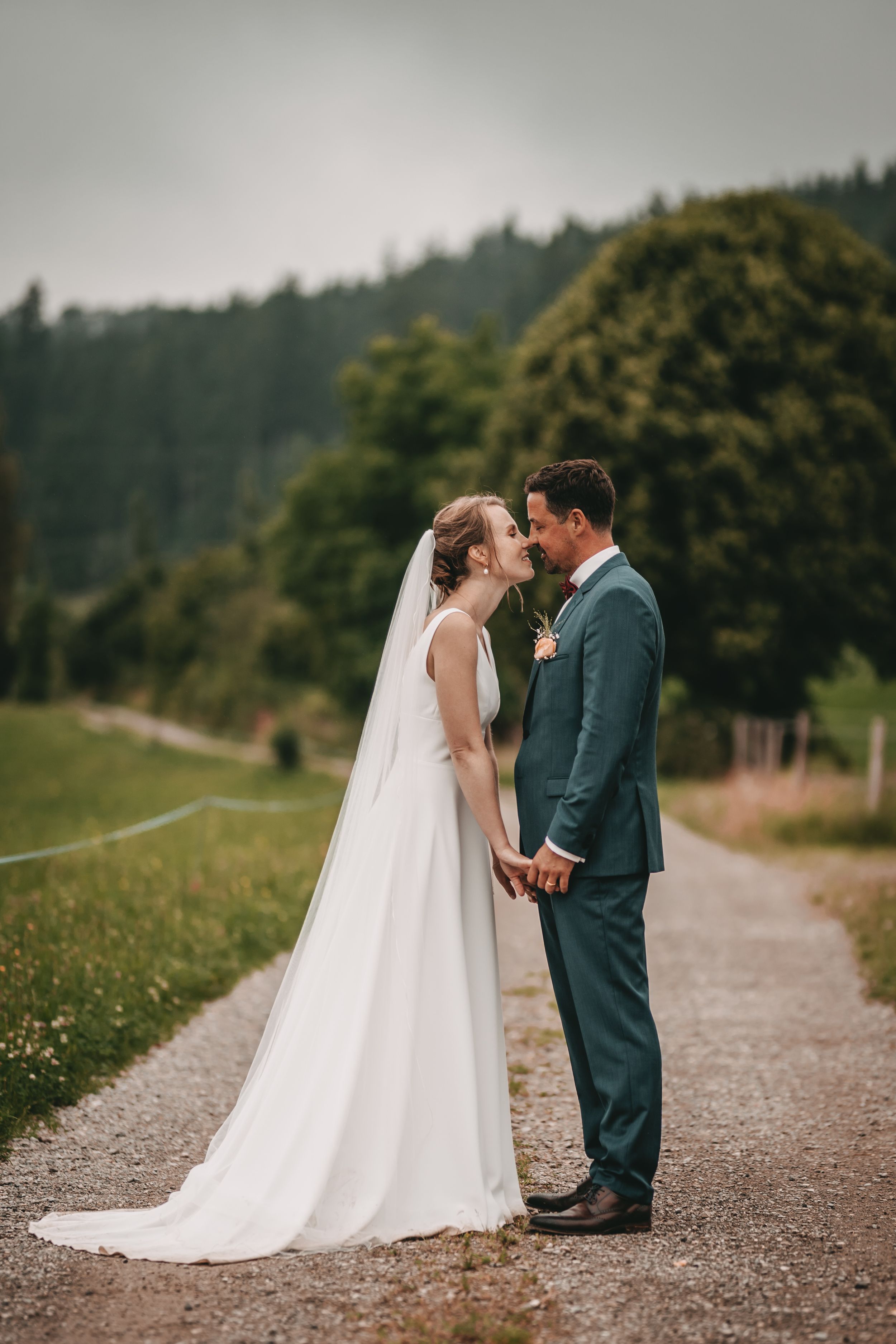 Wedding couple sharing an intimate moment on a gravel path with mountains and forest in the background.