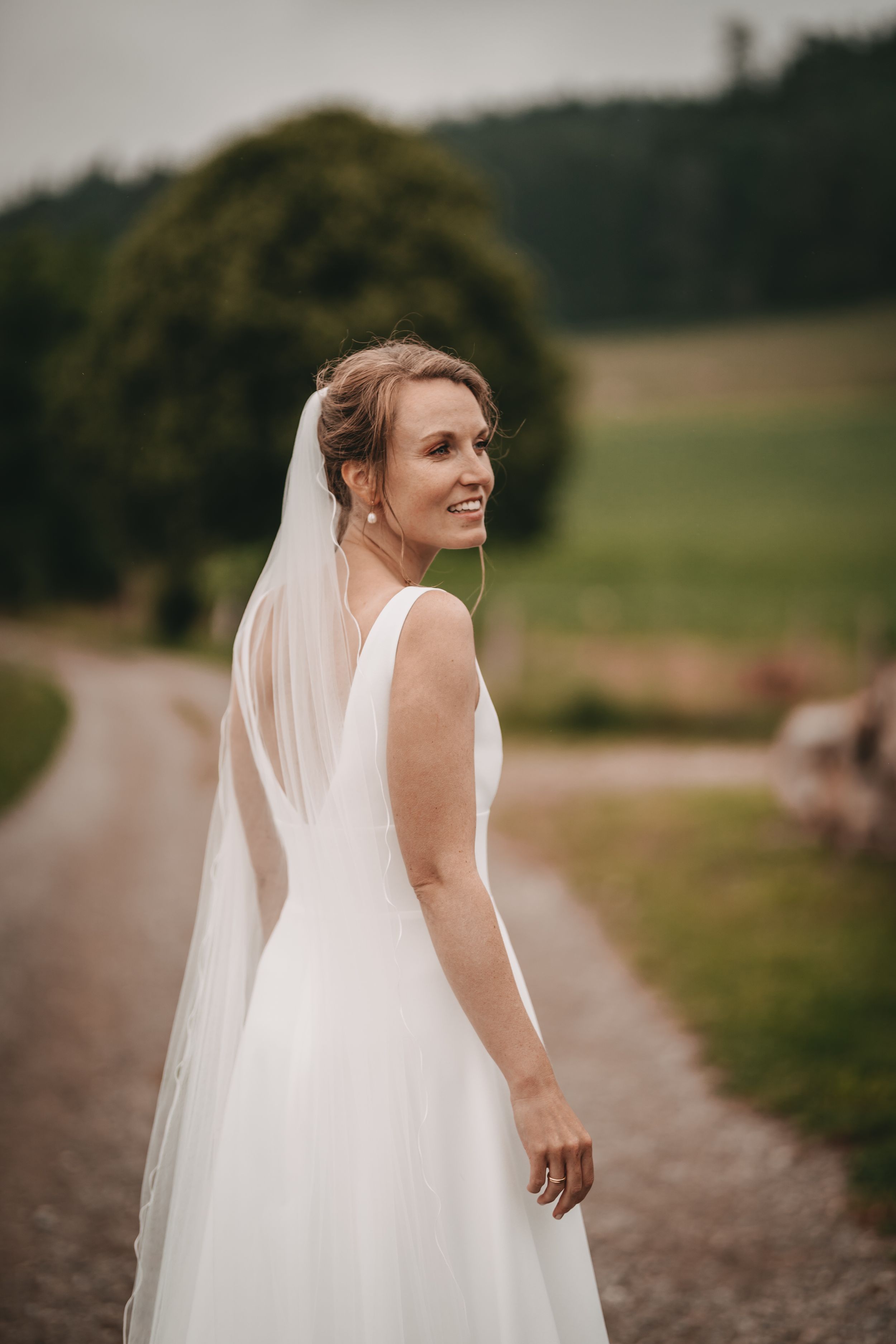 Bride in elegant white wedding dress and veil walking along a scenic mountain path.