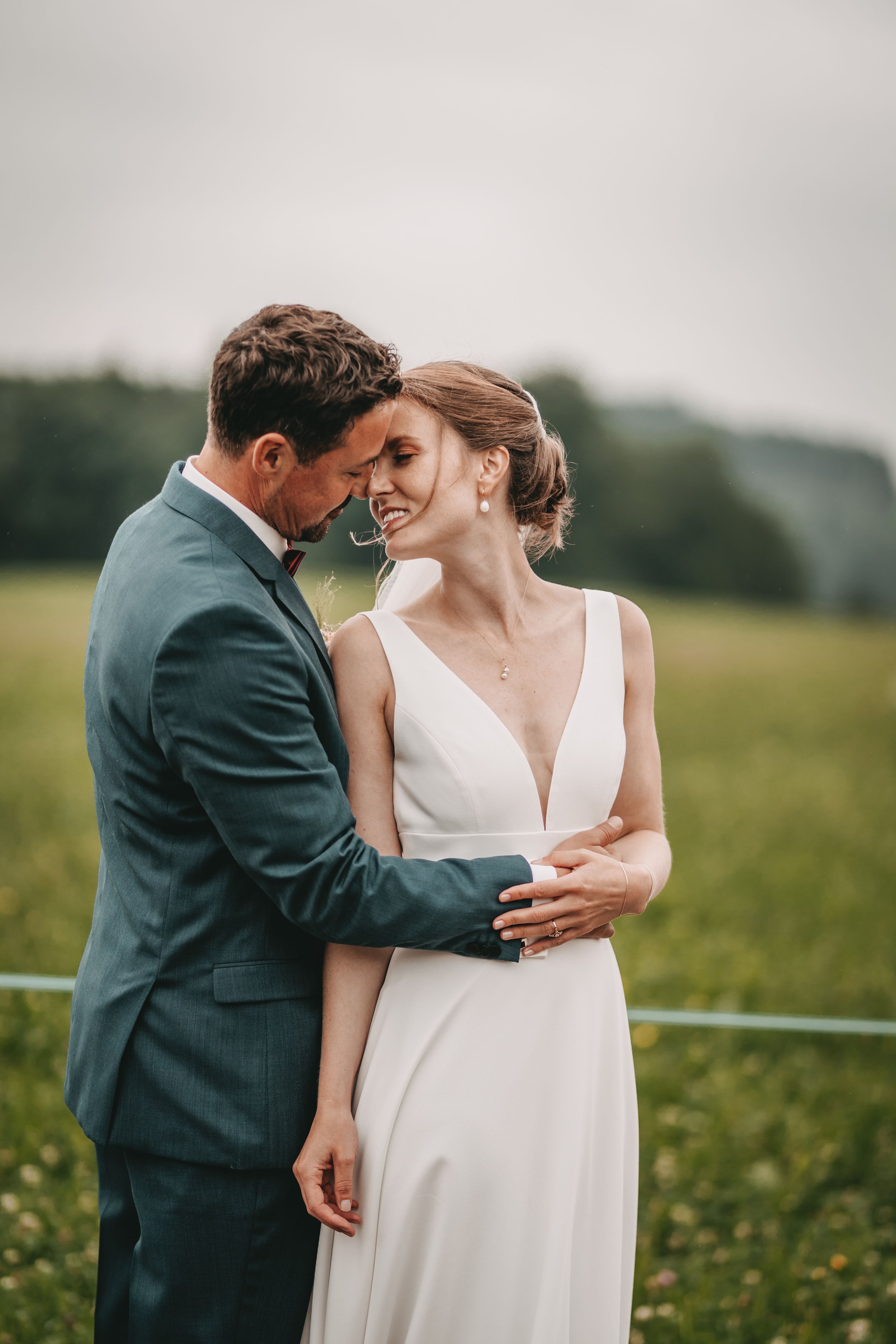 Intimate wedding couple moment captured in a green field against overcast sky.