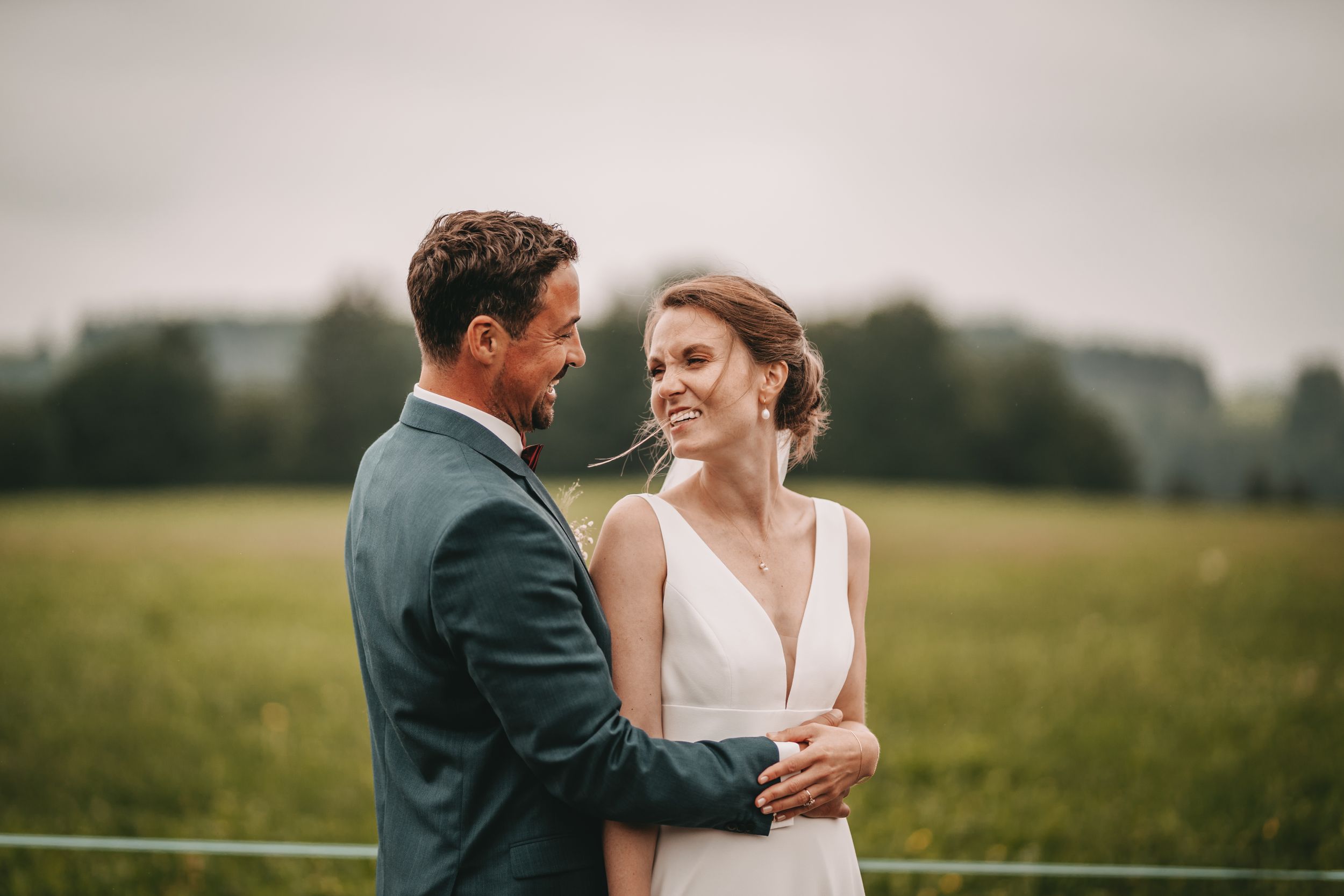 Joyful wedding couple sharing laughter in an outdoor field setting.