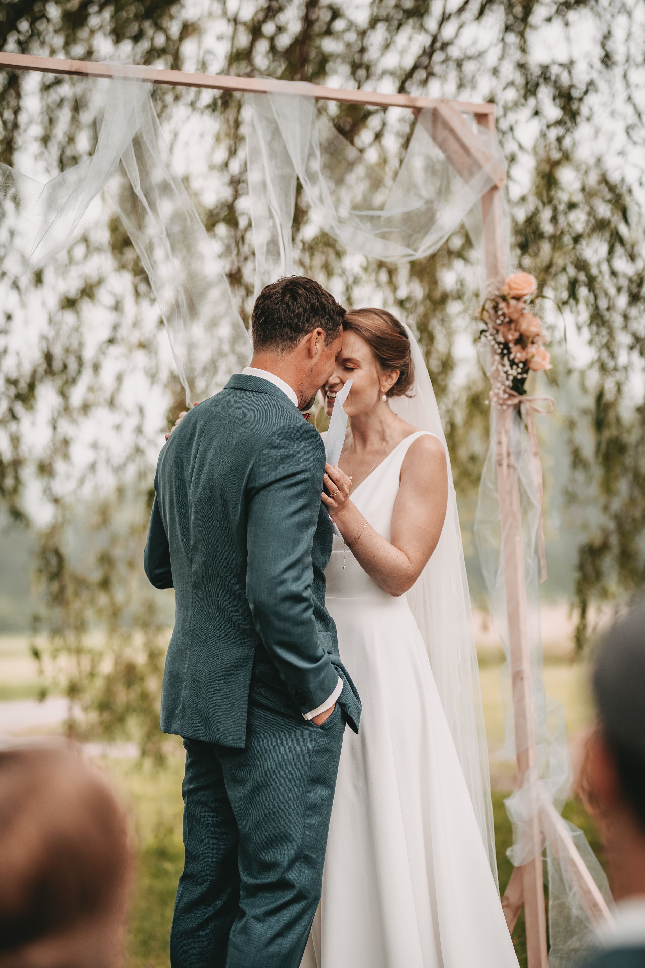 Intimate moment between bride and groom standing under a decorated wedding arch with flowing fabric.