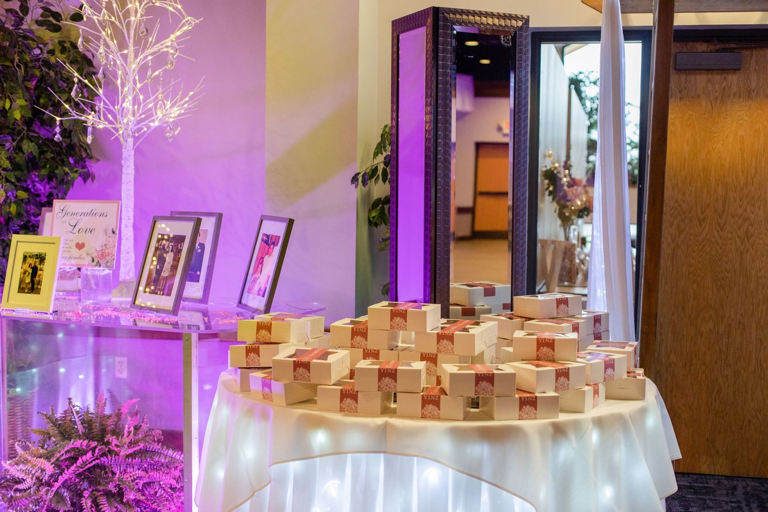 Wedding reception decor featuring illuminated white trees and purple ambient lighting.