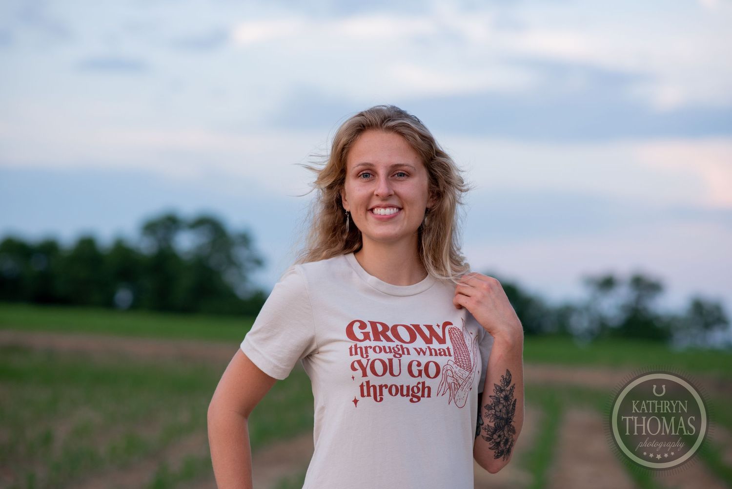 Smiling against sunset sky wearing white graphic t-shirt in farm field.