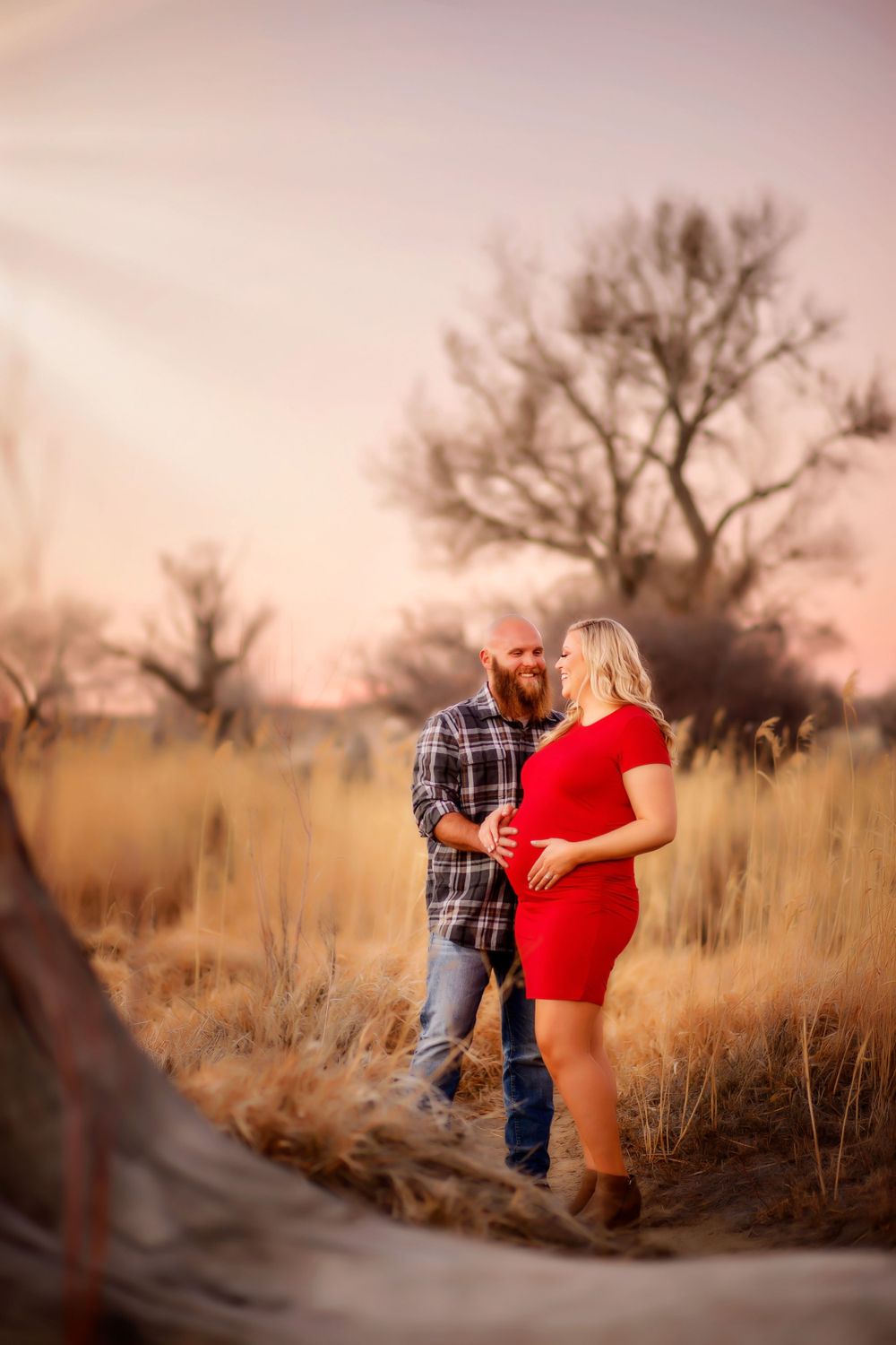 A couple shares an intimate moment during their maternity photoshoot in a natural setting.
