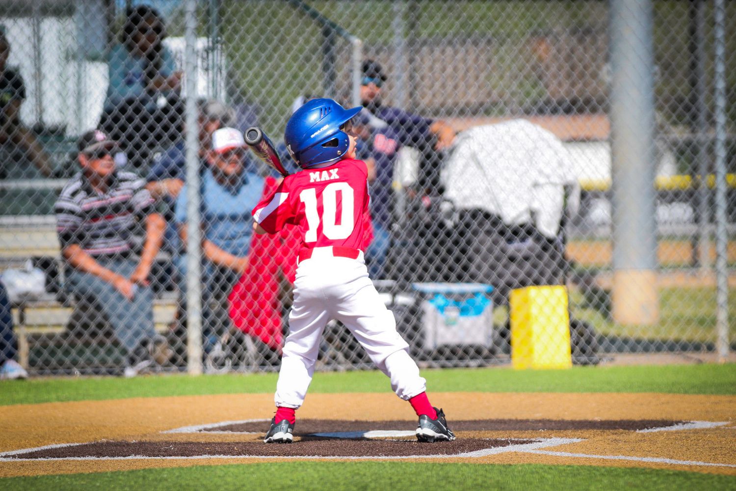 Youth baseball player in red uniform number 10 takes batting stance at home plate.