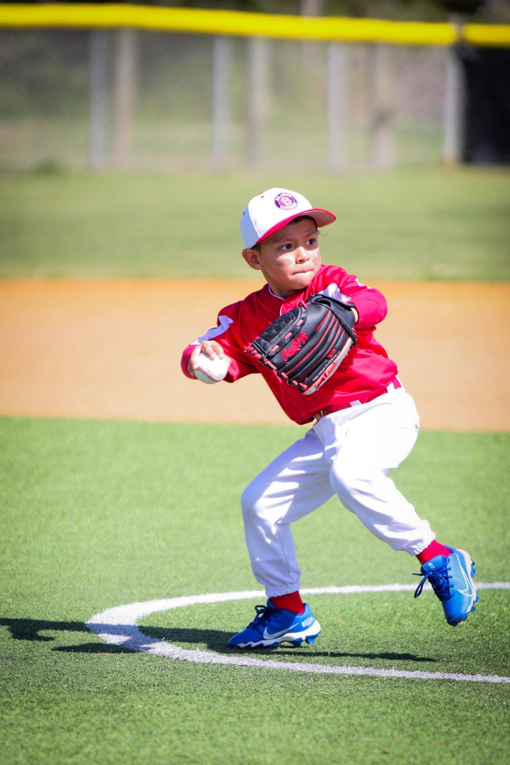 Young baseball player in red uniform practices fielding position on baseball diamond.