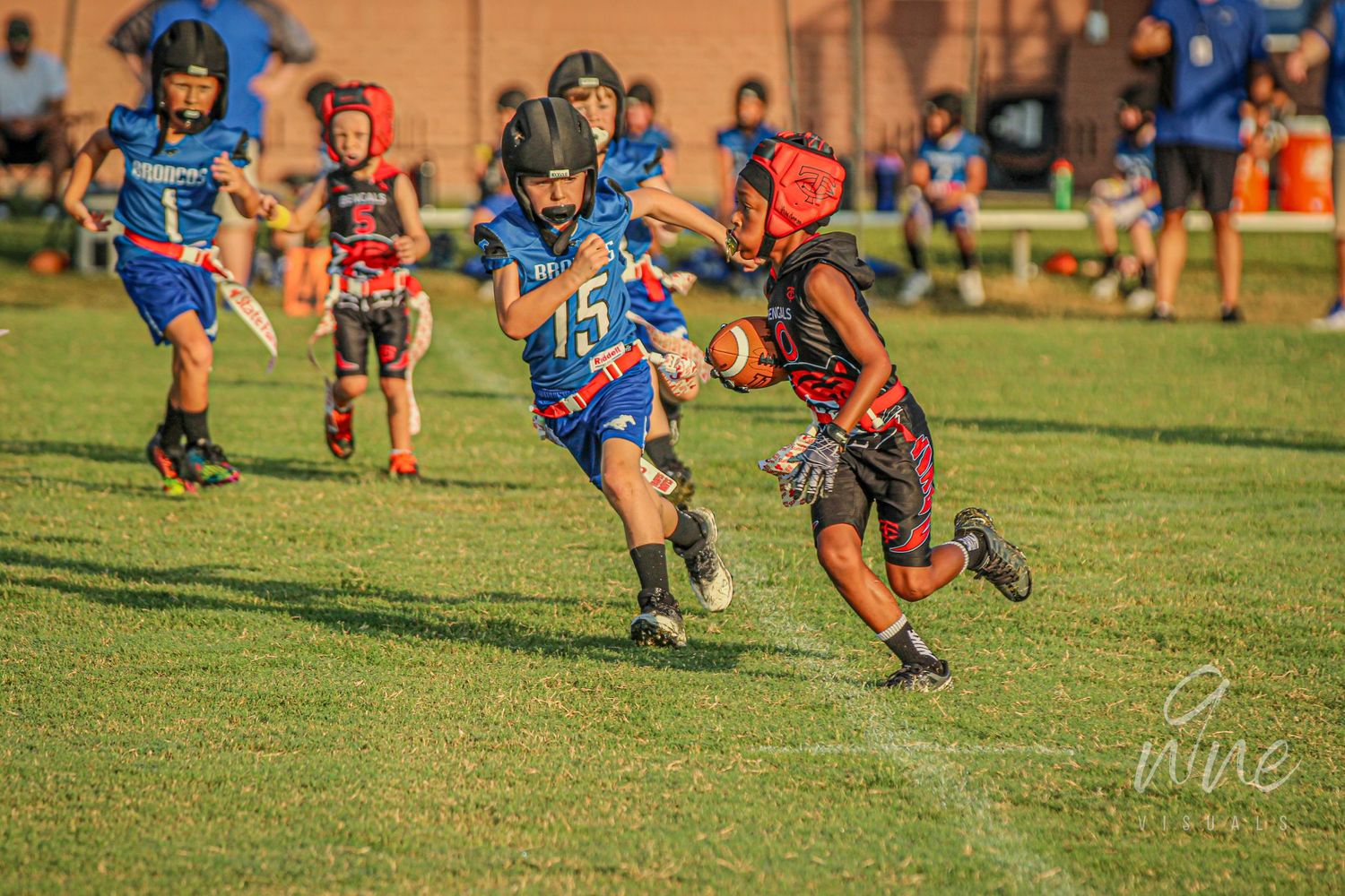Youth flag football game in action with players running across sunny field.
