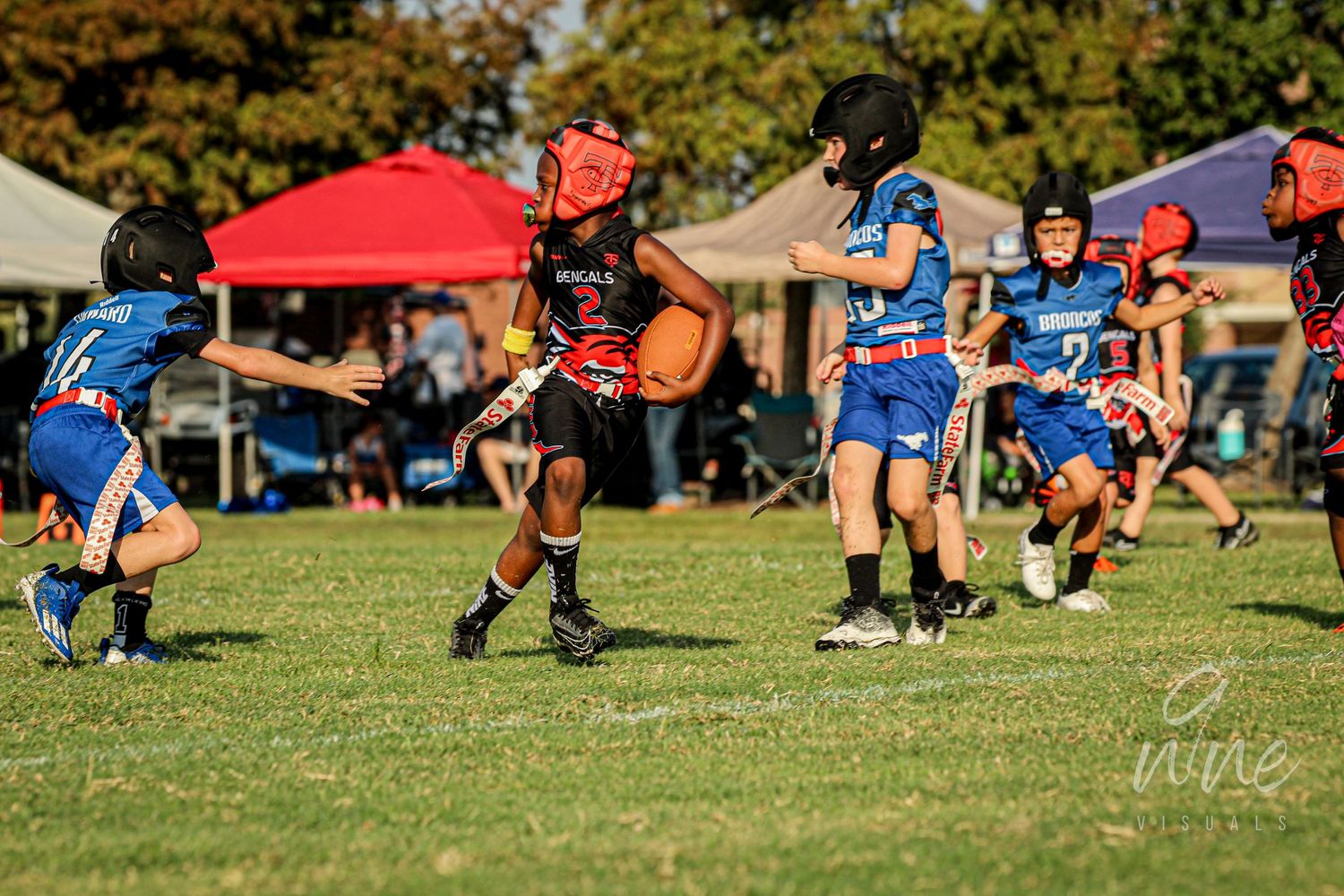 Dynamic flag football play with players leaping and running on grassy field.