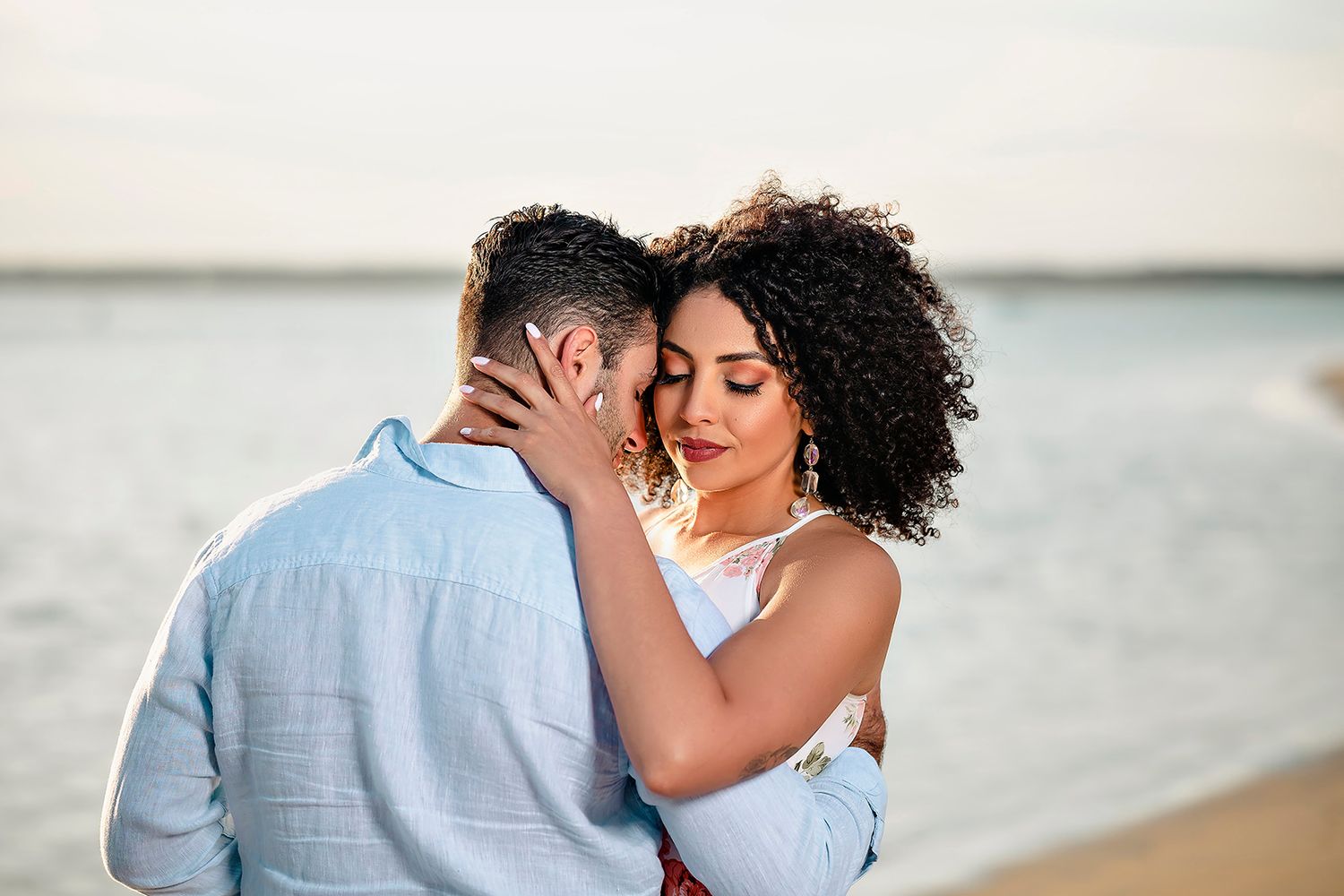 Romantic beach photoshoot with couple embracing against ocean backdrop at sunset.