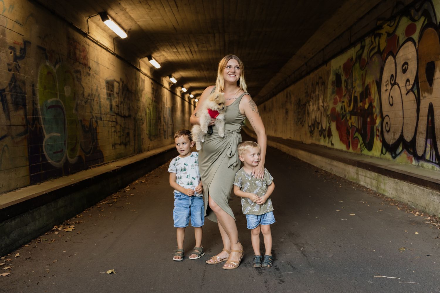 Family poses in urban tunnel with graffiti-covered walls and overhead lighting.
