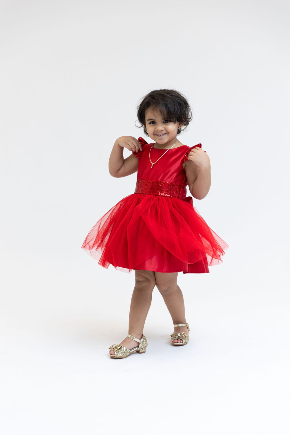 A sparkly red tulle dress twirls against a white studio backdrop.
