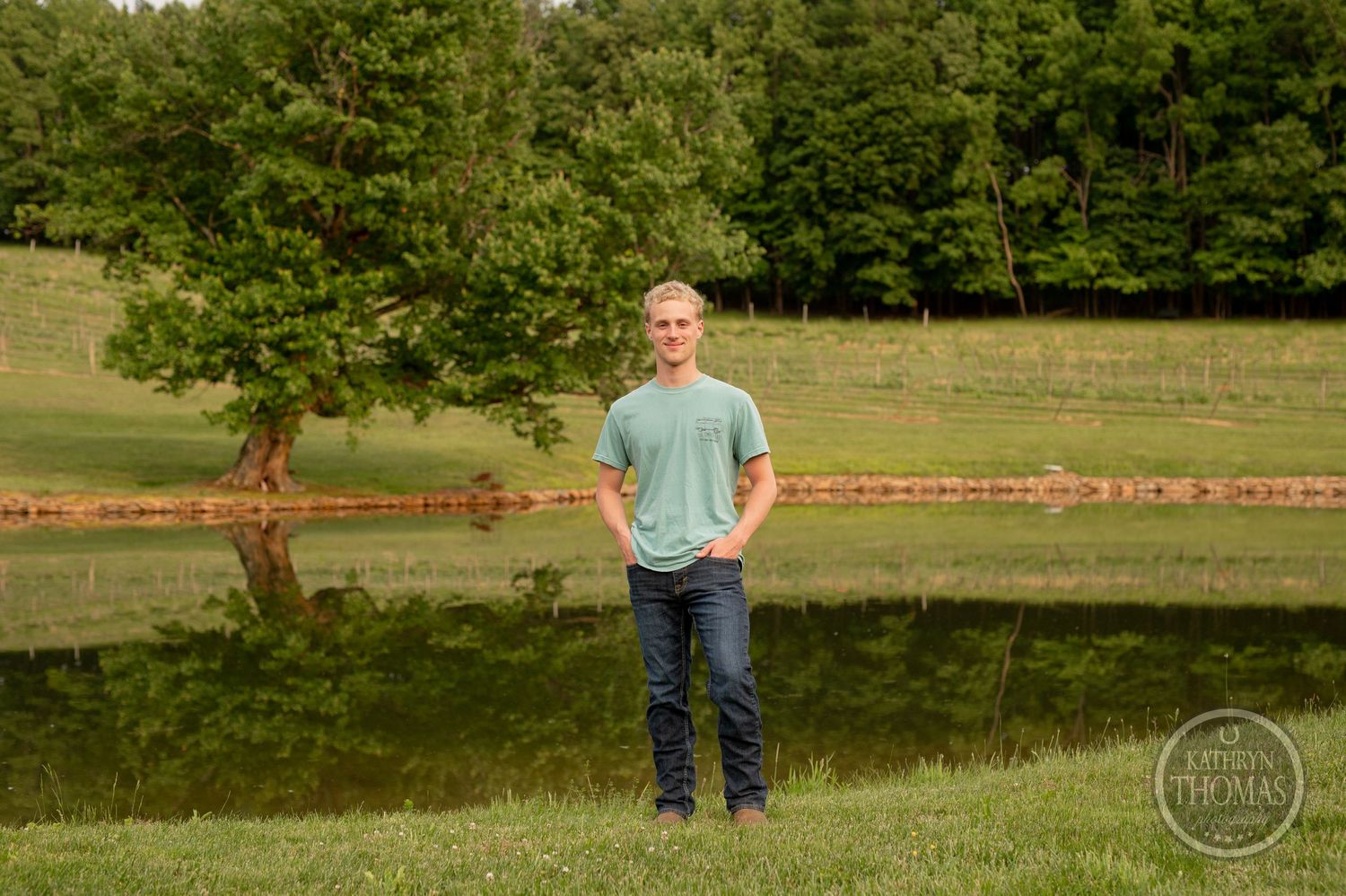 Person in mint t-shirt stands by peaceful pond with tree reflection.