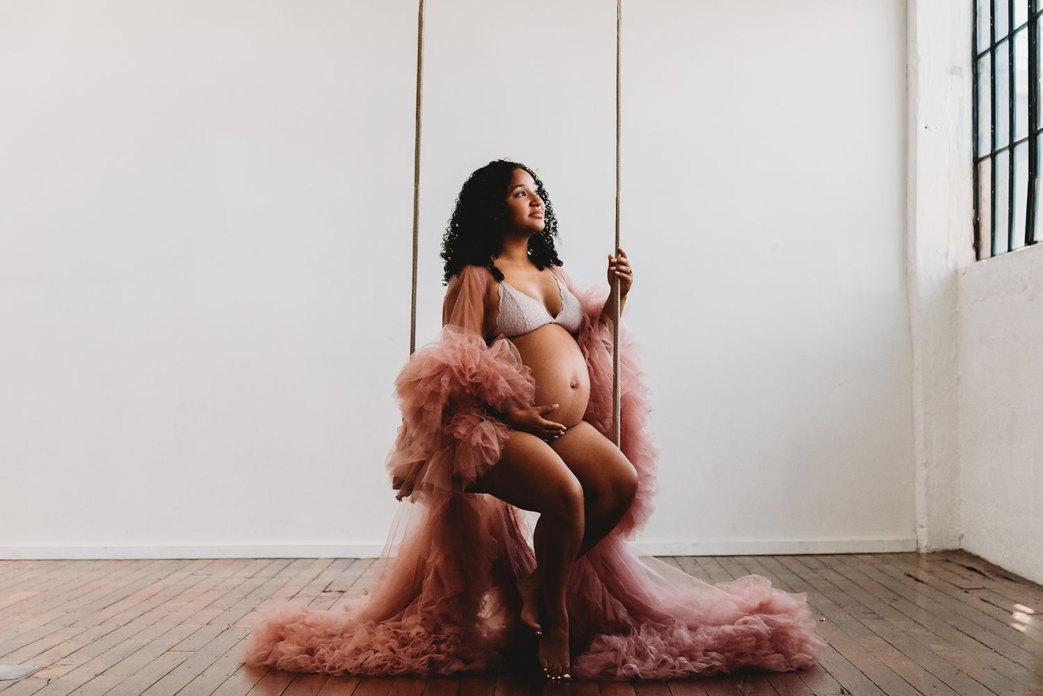 A maternity photo featuring flowing pink tulle fabric and artistic lighting in a minimalist studio.