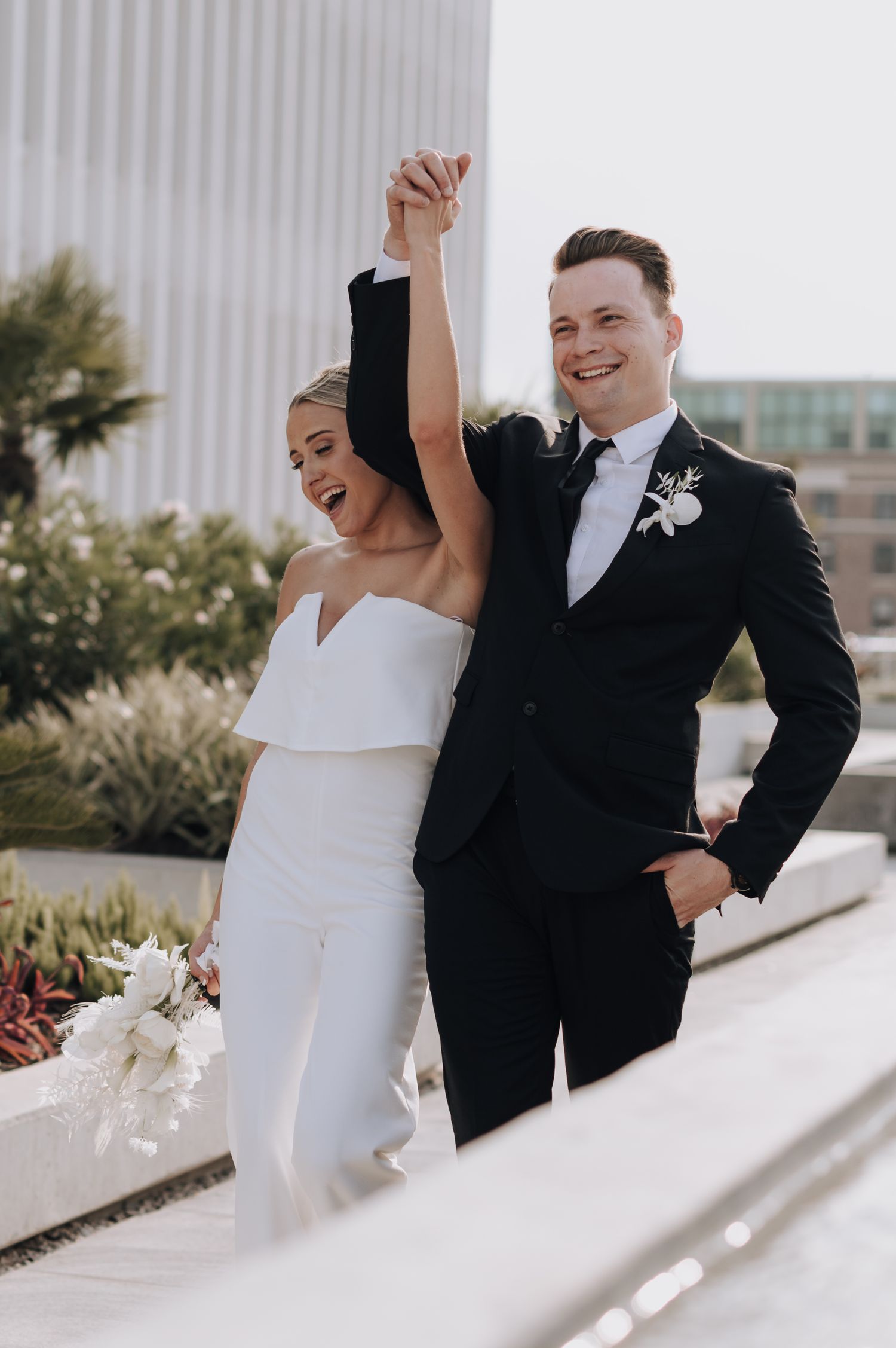 Joyful newlyweds celebrate with raised hands against modern architecture backdrop.