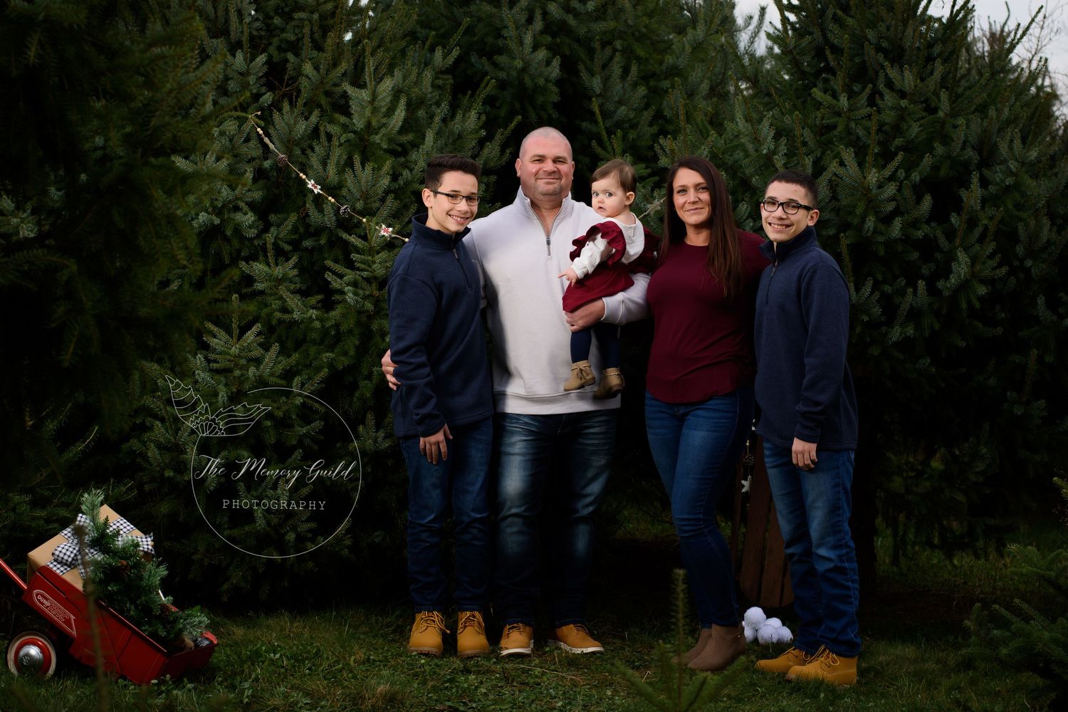 Family of five posing outdoors at a Christmas tree farm, smiling together for a holiday portrait photo.