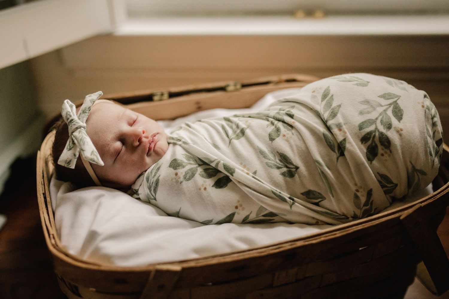 Sleeping newborn baby swaddled in floral print wrap lying in woven basket.