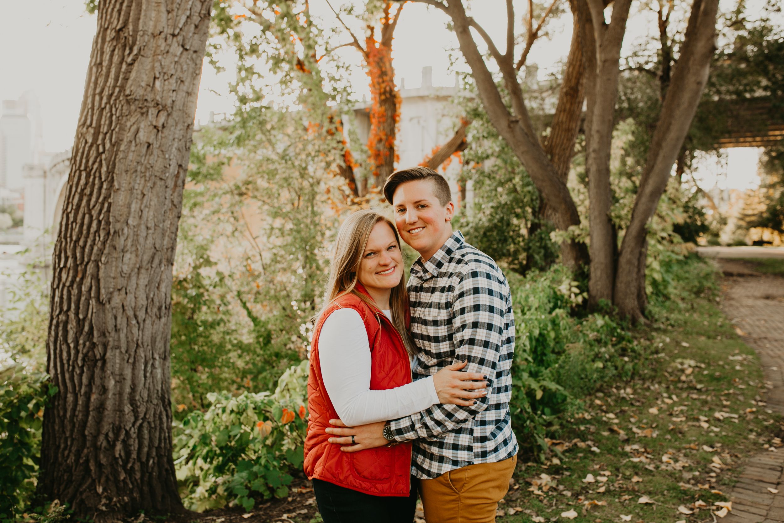 Couple embracing and smiling in a park during autumn with colorful foliage in the background.
