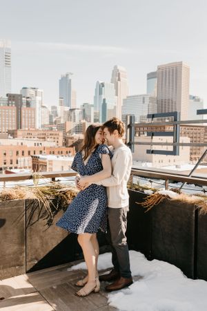 Couple sharing romantic moment on rooftop with city skyline backdrop on sunny winter day.