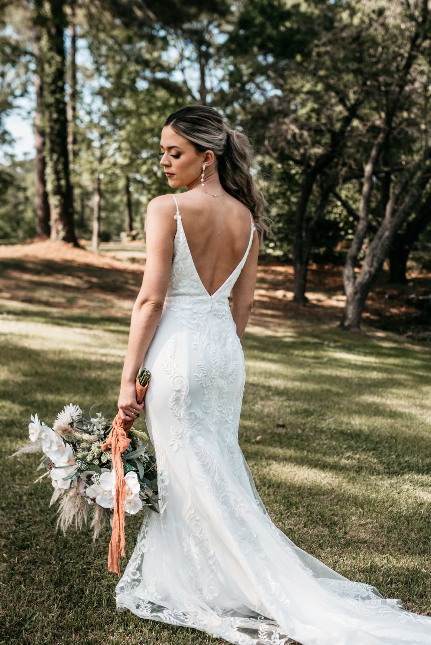 Elegant white lace wedding dress with deep V-back photographed outdoors with a rustic bouquet.