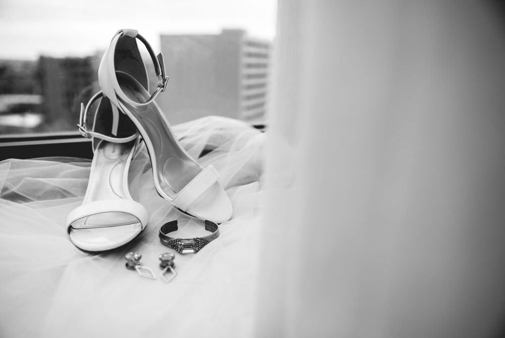 Elegant white bridal heels and jewelry arranged on a windowsill in black and white.
