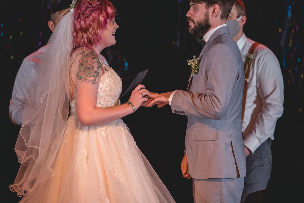 A couple exchanges rings during their wedding ceremony on a dimly lit stage.