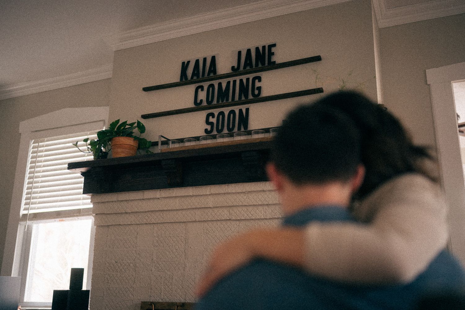 Sign reading 'KAIA JANE COMING SOON' mounted on wall above window with decorative plants.