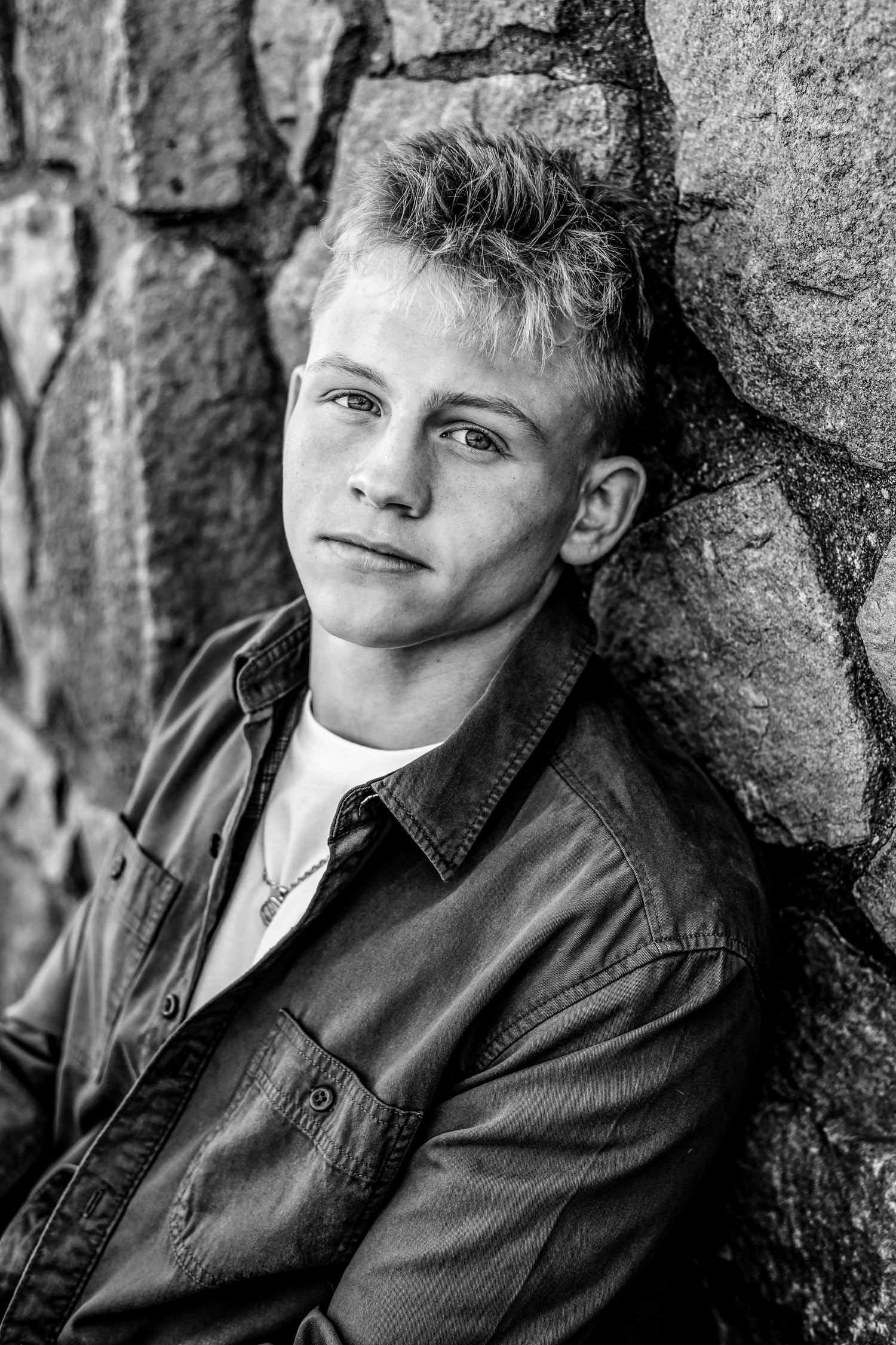 Black and white portrait of person leaning against stone wall.