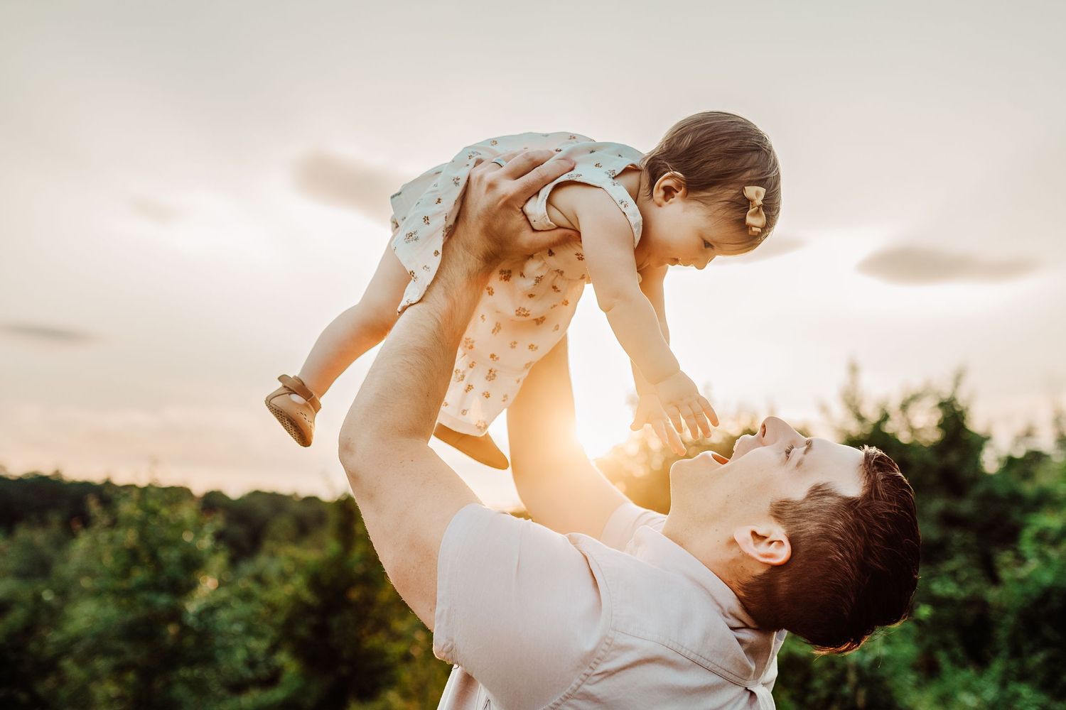 Parent lifting happy child against golden sunset sky outdoors.