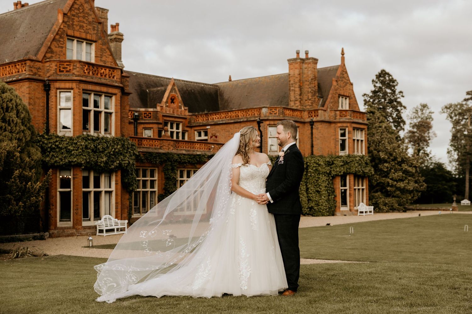 Wedding couple poses in front of historic brick mansion on overcast day.