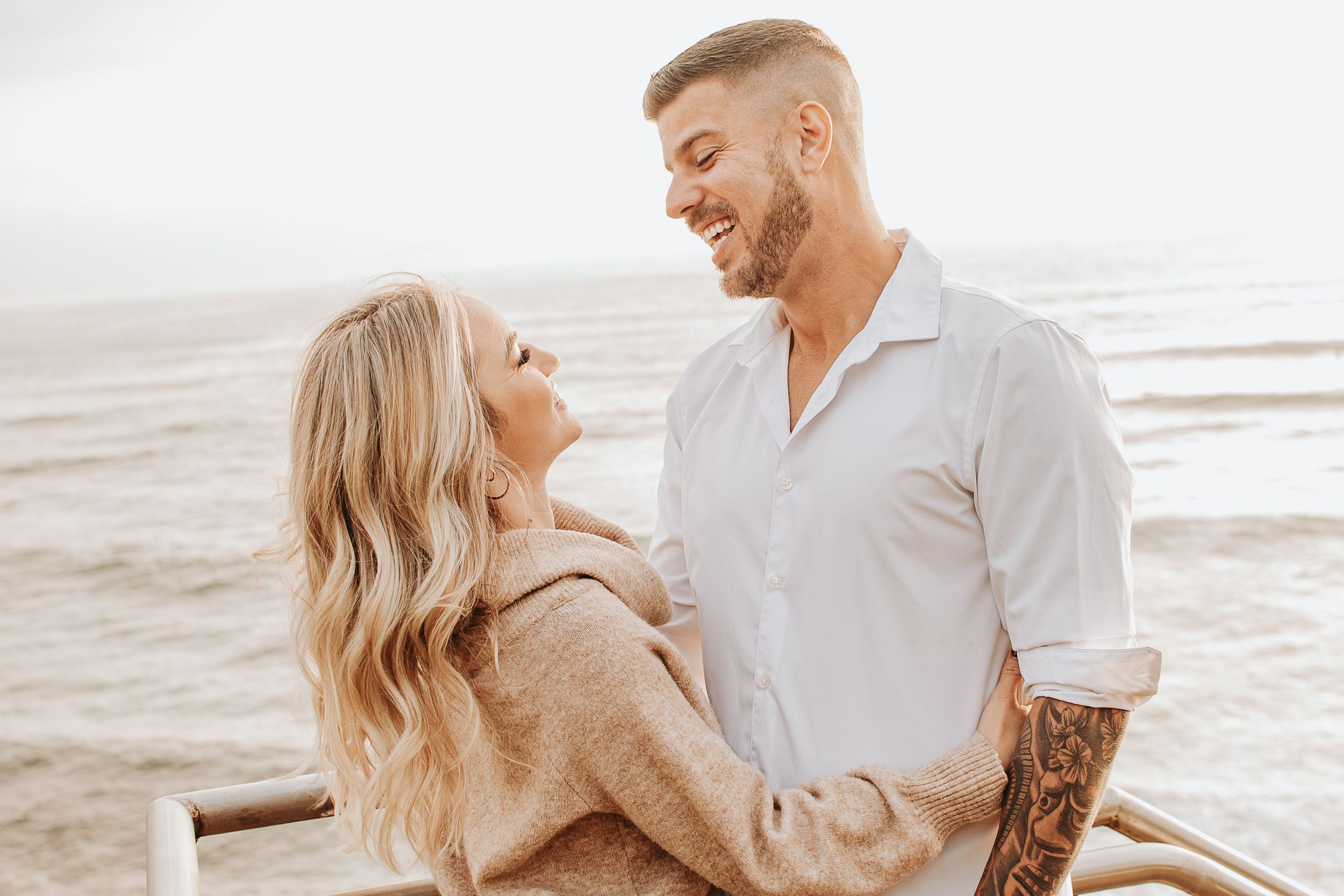 Couple in casual beach attire sharing tender moment by the ocean.