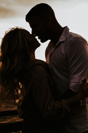 A silhouetted couple sharing an intimate moment at sunset against a warm backlit sky.