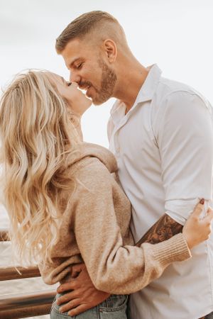 A romantic couple embracing by the ocean while wearing casual attire.