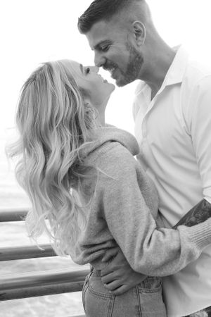 A black and white portrait of a couple sharing a tender moment by the sea.