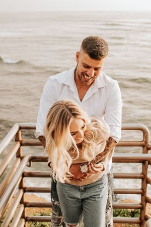 A couple sharing a candid moment together on coastal stairs during golden hour.