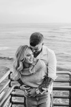 A black and white image of a couple embracing on oceanside steps.