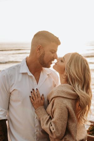 A romantic couple in white and beige sharing an intimate moment by the ocean at sunset.