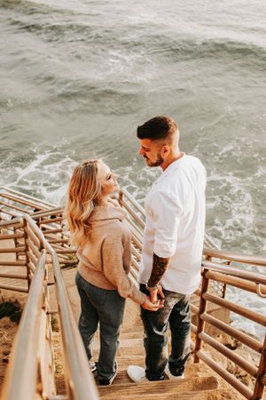 Couple standing on oceanside boardwalk sharing intimate moment at sunset.