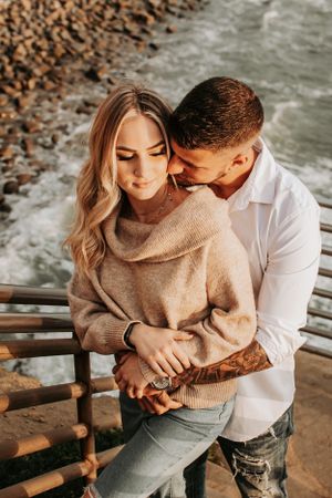 Romantic embrace on coastal walkway with waves crashing in background.