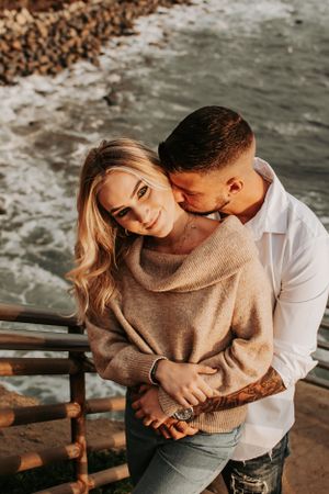 Tender moment shared between couple on seaside walkway during golden hour.