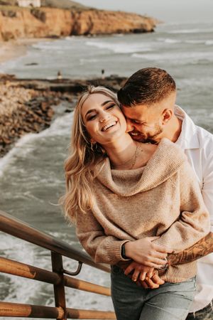 Playful couple sharing laughter and embraces by coastal cliffs.