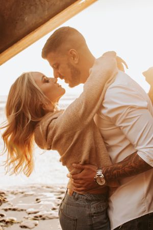 Romantic couple embraces in golden sunlight against rocky backdrop during sunset photoshoot.