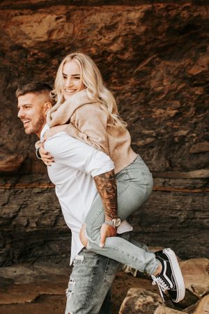 Playful couple having fun with piggyback ride against rocky cliff background.
